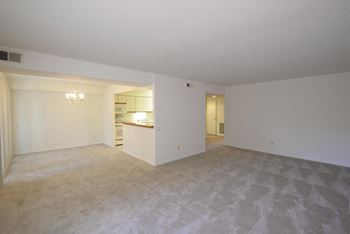 An empty living room with a kitchen in the background